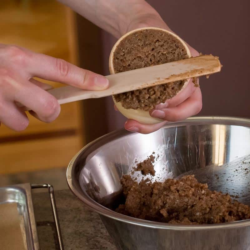 Überschüssiger Teig aus einer LebkuchenGlocke wird abgestrichen, darunter eine Schüssel mit Lebkuchenteig.