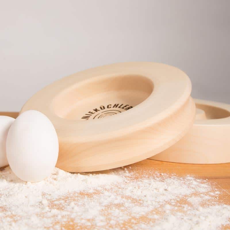 Bild von Knieküchler auf einem Holztisch, Nahansicht, davor ein Ei in Mehl