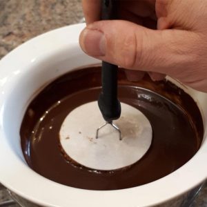 Dreizack sticht in Backoblate, die in eine Schüssel mit Schokoladenglasur getaucht ist.