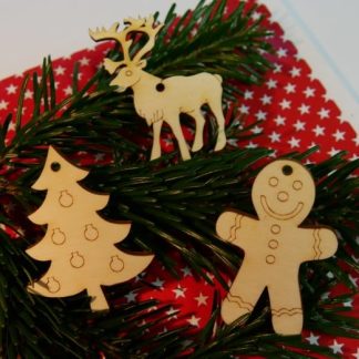 Drei Geschenkanhänger aus Holz in "Rentier", Tannenbaum", "Person" vor grünem Nadelzweig auf rot-weißer Weihnachtsunterlage mit Sternen.