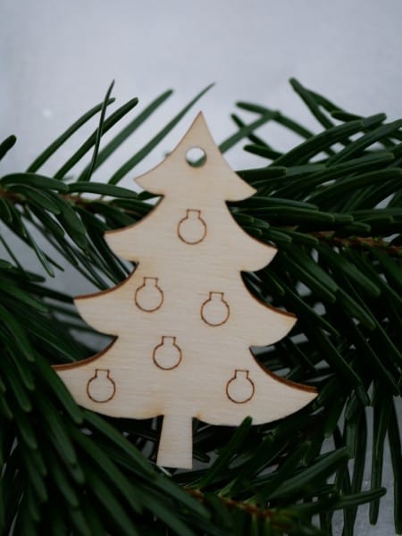 Geschenkanhänger aus Holz in "Tannenbaumform" vor grünem Nadelblatt